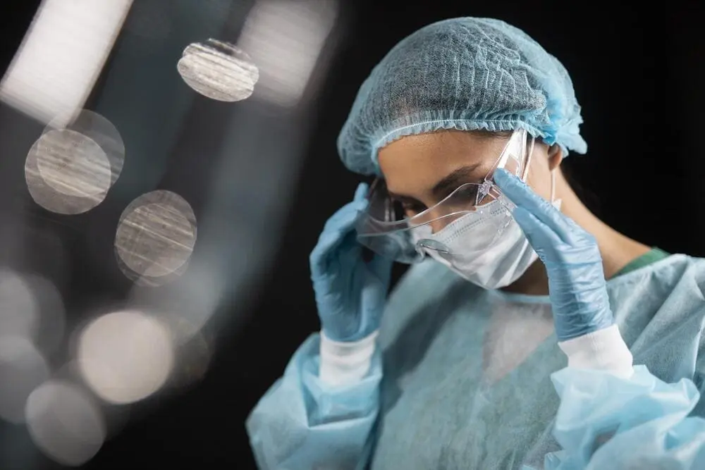 infirmiere de bloc opératoire enlevant ses lunettes de protection après l'opération